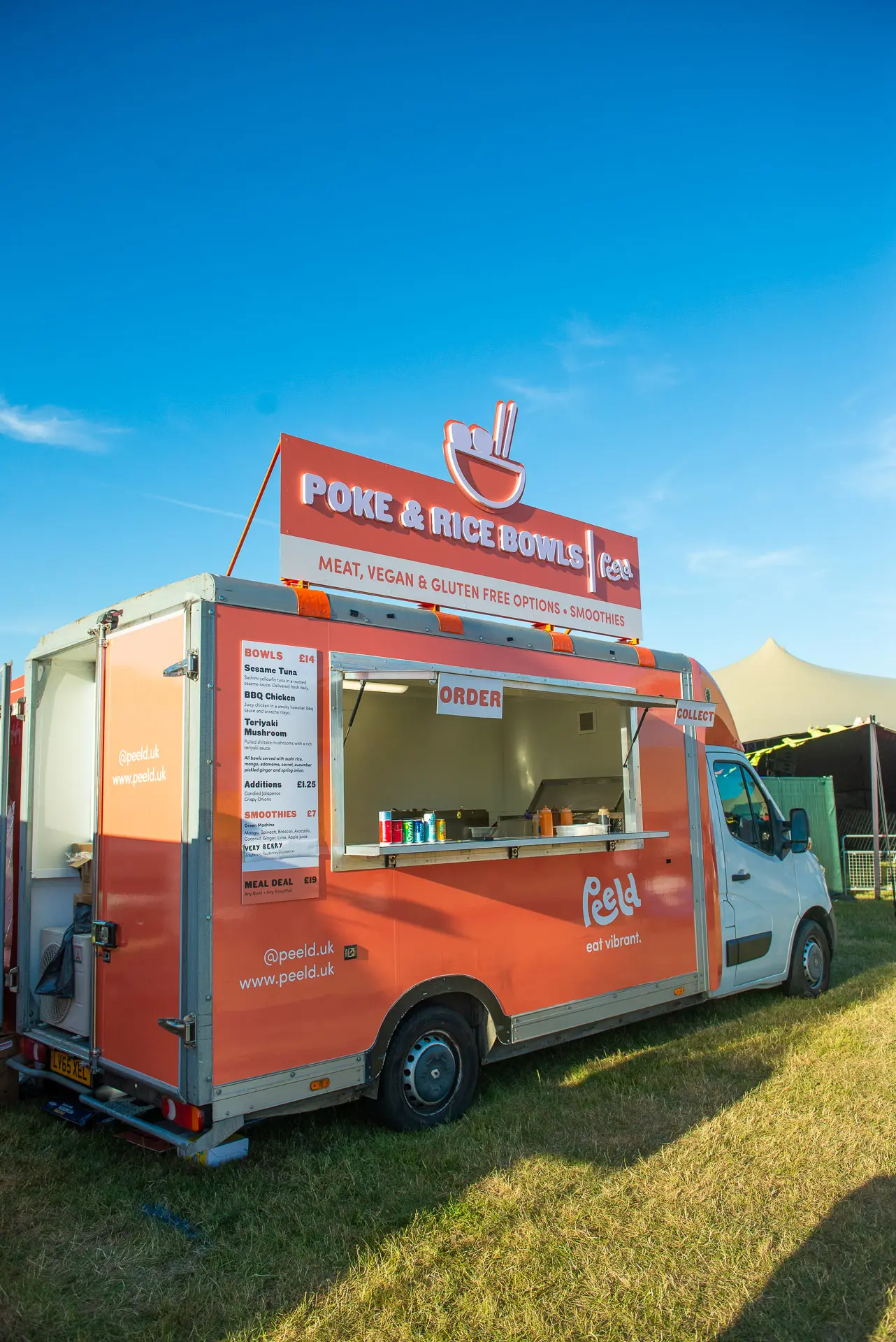 Bertha, the salmon-coloured Peeld food truck, parked on a festival field under a blue sky